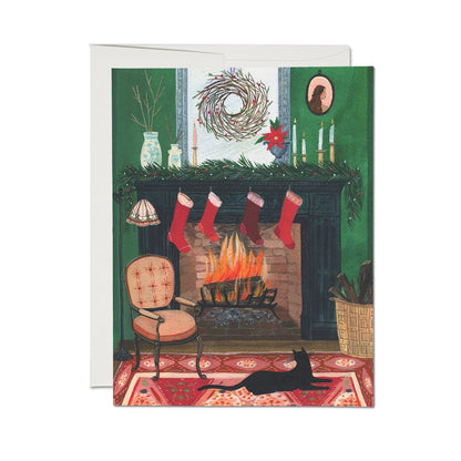 Christmas card with a fireplace, stockings, and a cat on a red rug.