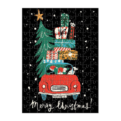 A completed jigsaw puzzle featuring a festive Christmas illustration: a red vintage car carrying a tall green Christmas tree and stacked gift boxes, on a black background with white snow-like specks and the words 'Merry Christmas!' at the bottom.