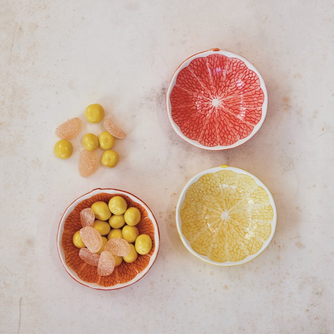 Citrus fruit shaped bowls with snacks in them on a marble surface