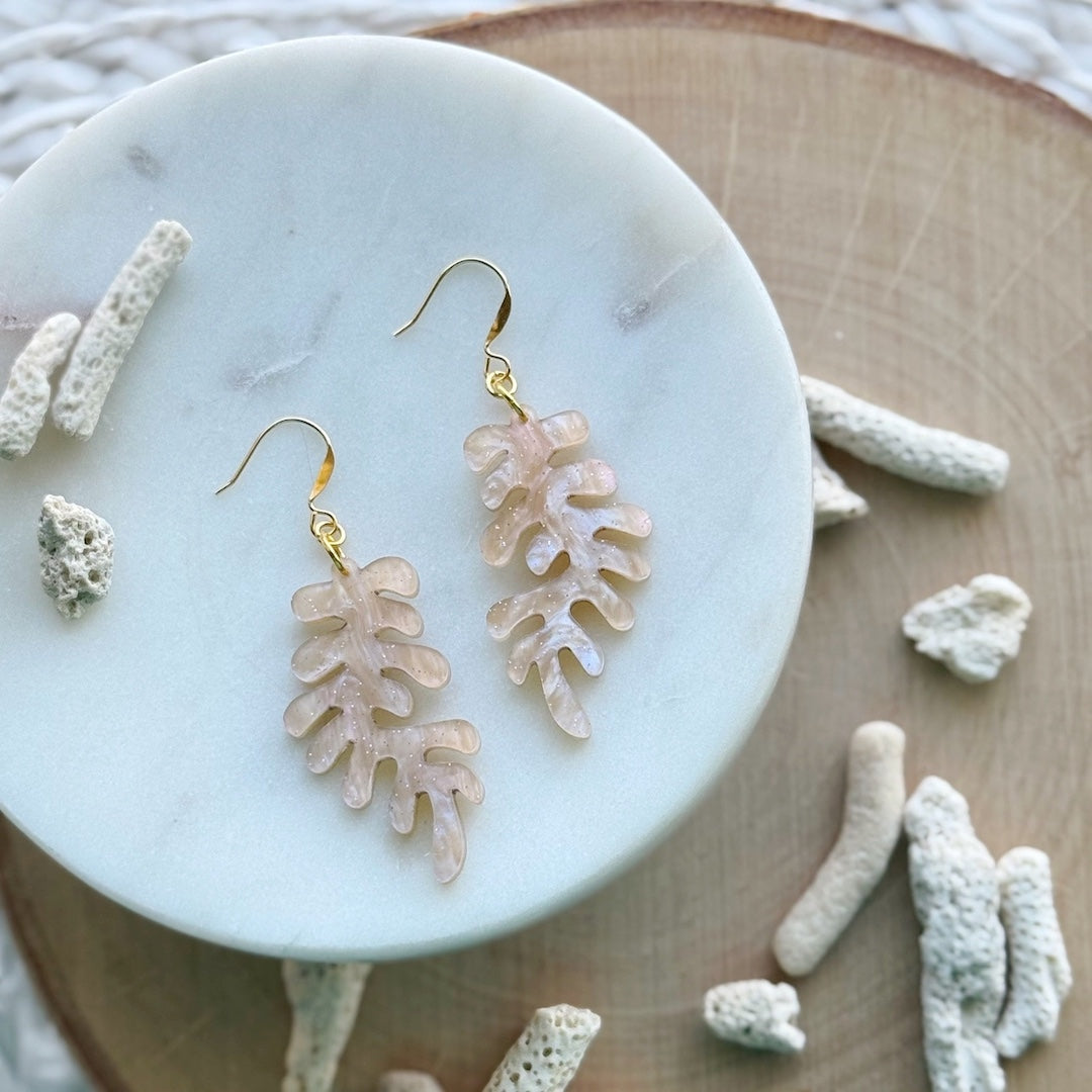 light pink Coral-shaped earrings on a marble surface with coral decorations.