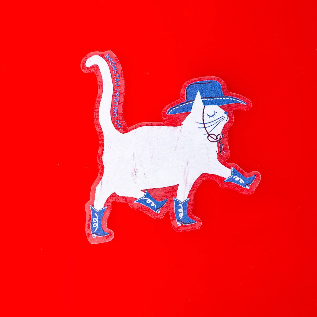 Sicker of a white cat wearing a blue cowboy hat and blue cowboy boots on a red background