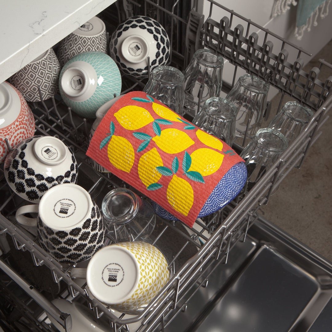 Dishwasher with a colorful lemon-patterned Swedish dishcloth on a rack filled with dishes.