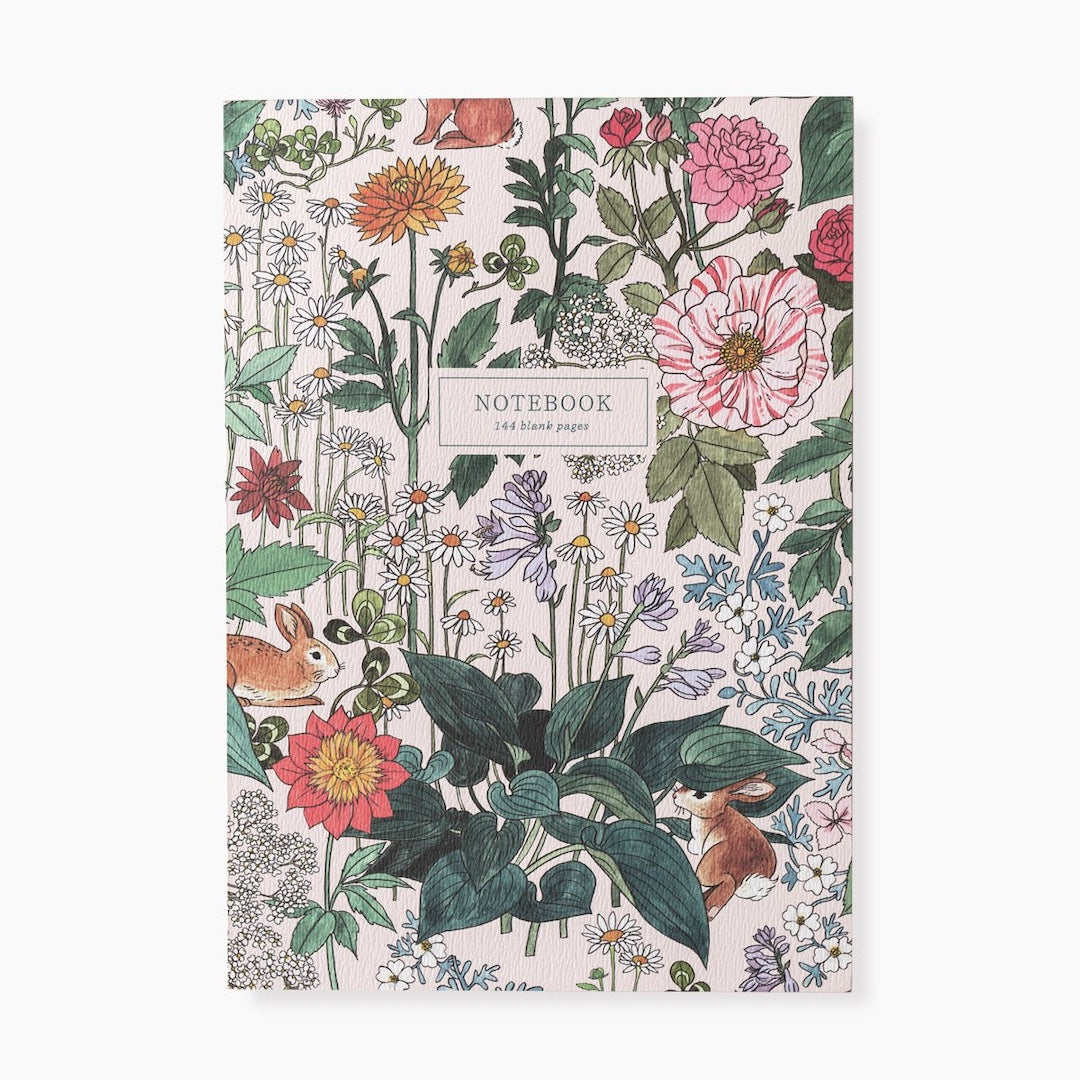 The front cover of a notebook. The notebook has a white background with a whimsical nature inspired pattern featuring flowers, leaves, bunnies, and a small box that has "notebook" and "144 blank pages" written in it. Shown on a white background.