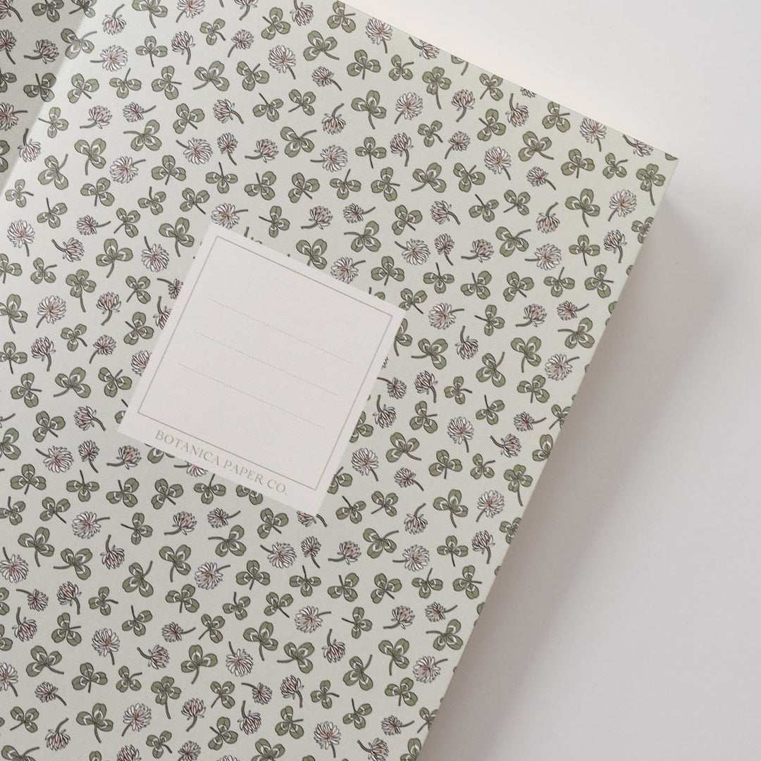 A page that has clovers and flowers on it. In the middle of the page is a box with 3 lines and "Botanica Paper Co." written at the bottom of the box.