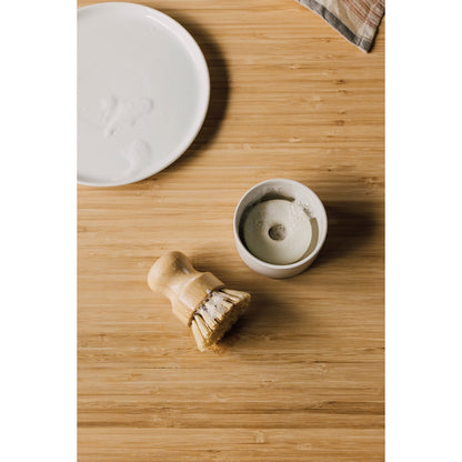 Ceramic bowl with soap in it, small dish brush brush, and plate on a wooden surface