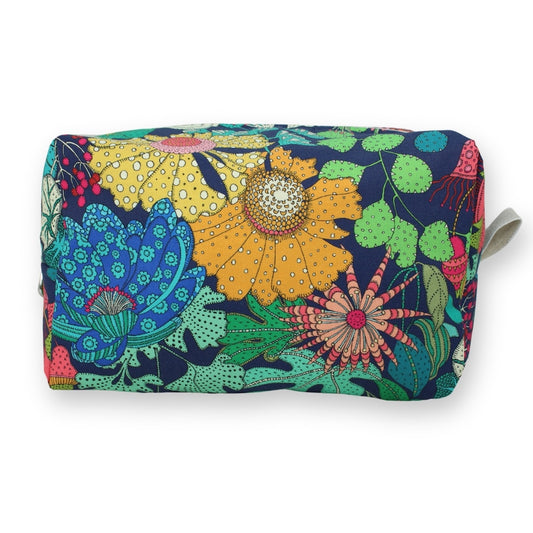 A rectangular cosmetic pouch with a colorful, busy floral and botanical pattern on a navy blue background, featuring a small white strap on the right side.