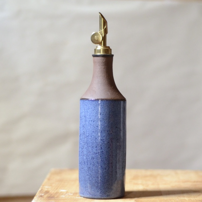 two-tone brown and blue ceramic oil bottle with a gold nozzle on a wooden surface
