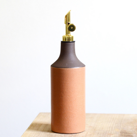 Two-toned brown and peach ceramic oil bottle with brass nozzle on a beige surface.