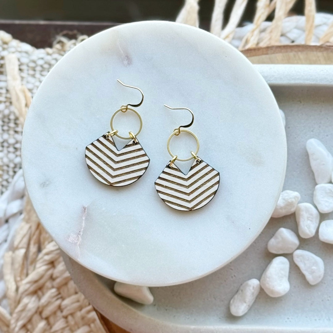 Pair of dark brown and white chevron patterned earrings hanging off a brass circle on a marble surface.
