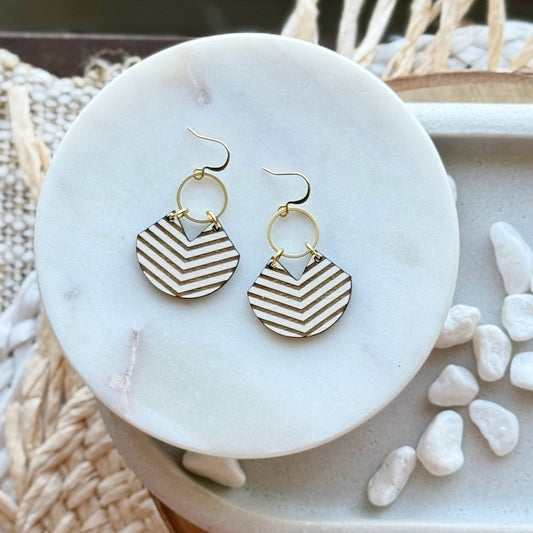 Pair of dark brown and white chevron patterned earrings hanging off a brass circle on a marble surface.
