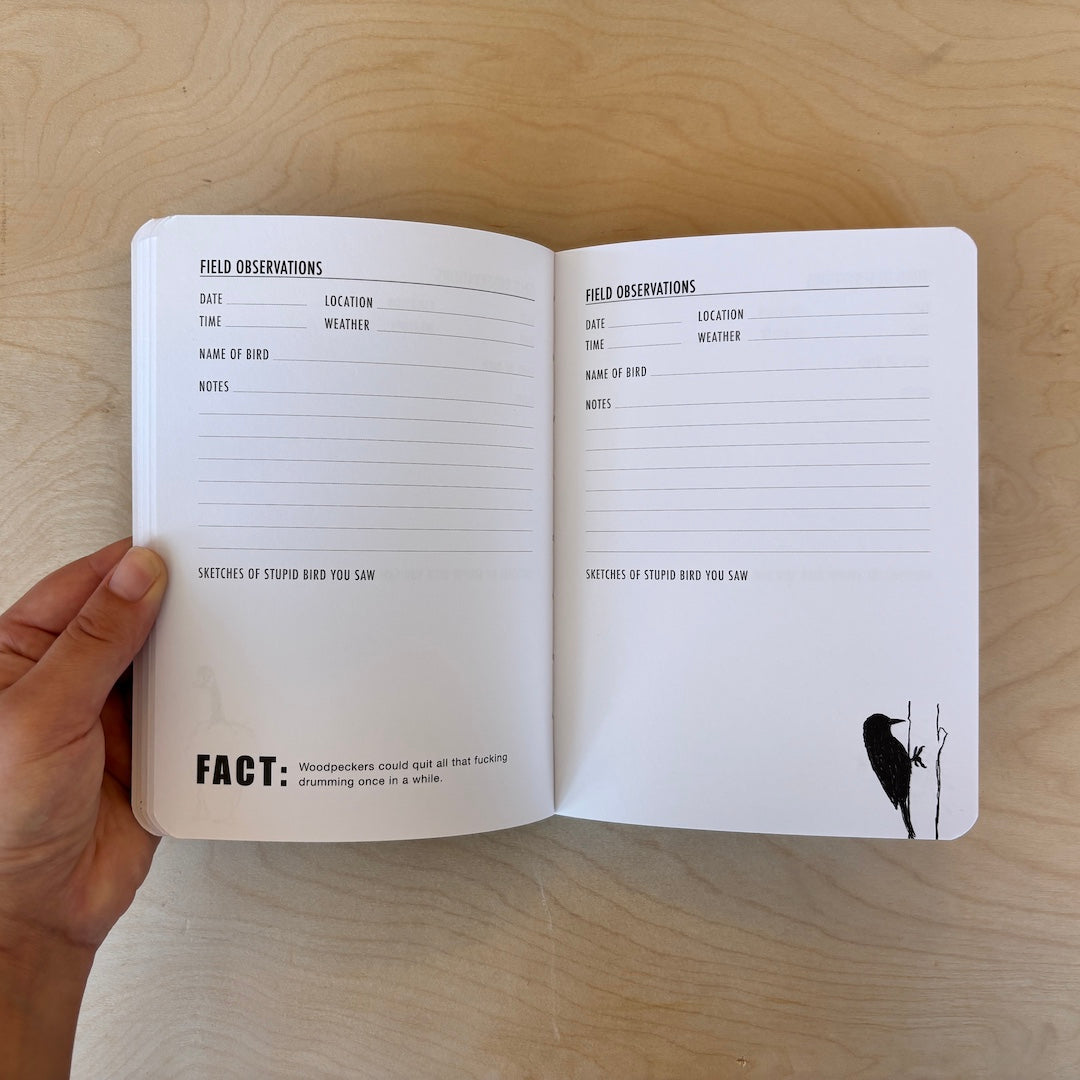 An open bird journal with printed observation pages held in a hand over a light wood surface. The pages contain sections for about the weather, name of bird, notes, location, time, and a space to sketch the bird