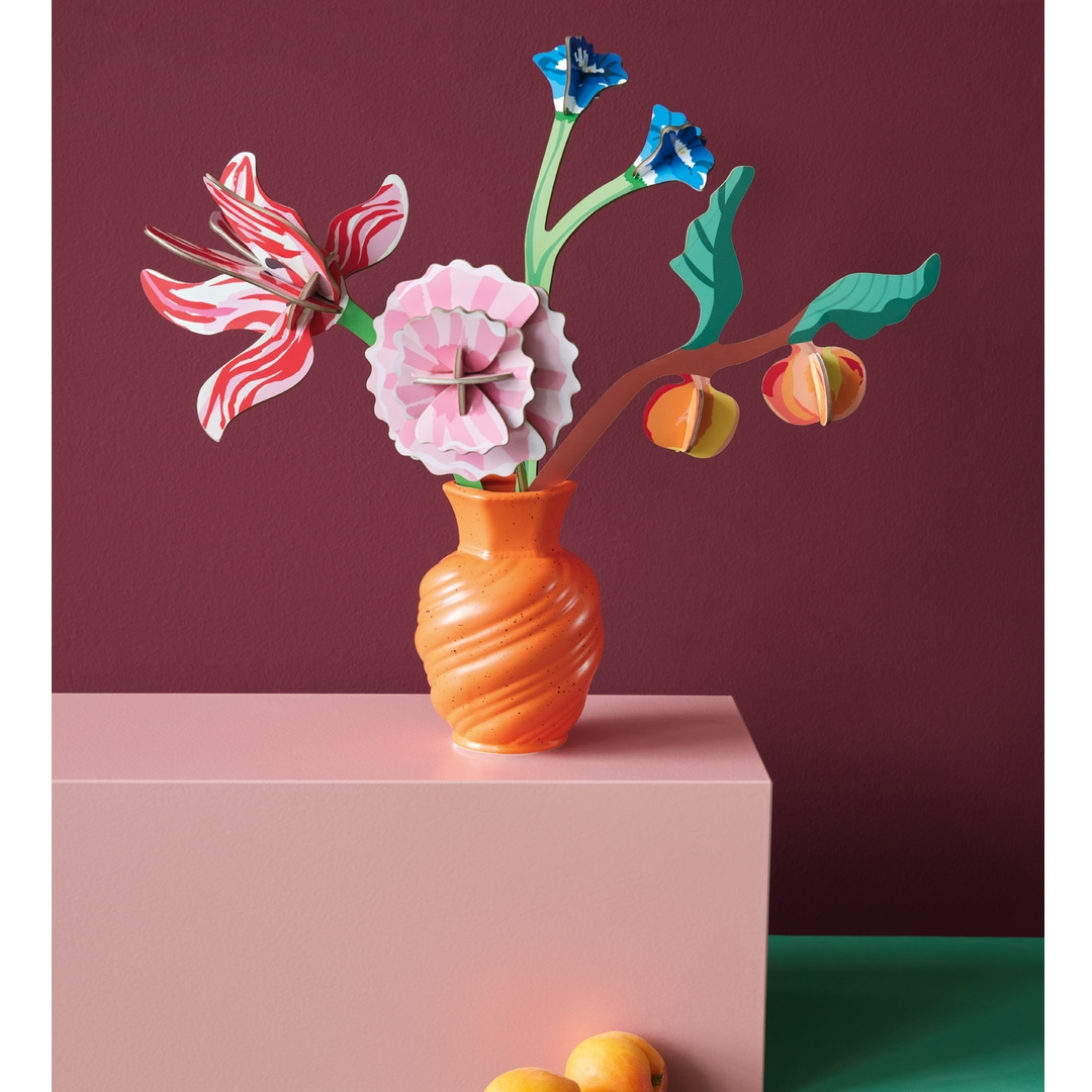 Colorful floral arrangement in an orange vase on a pink platform with a dark red background