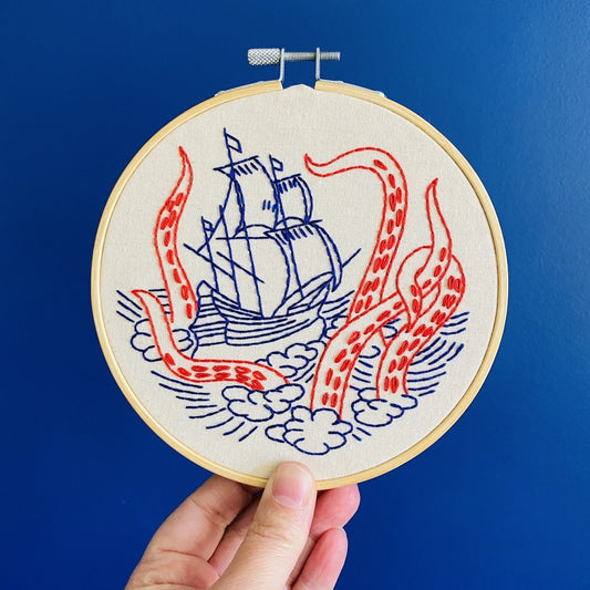 Embroidery hoop with a ship and tentacle design against a blue background