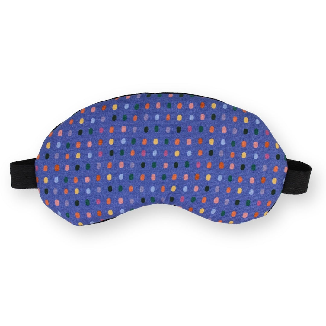 A sleep mask with a purple base and a colorful pattern of small, colored dots, featuring black adjustable straps on a plain white background.