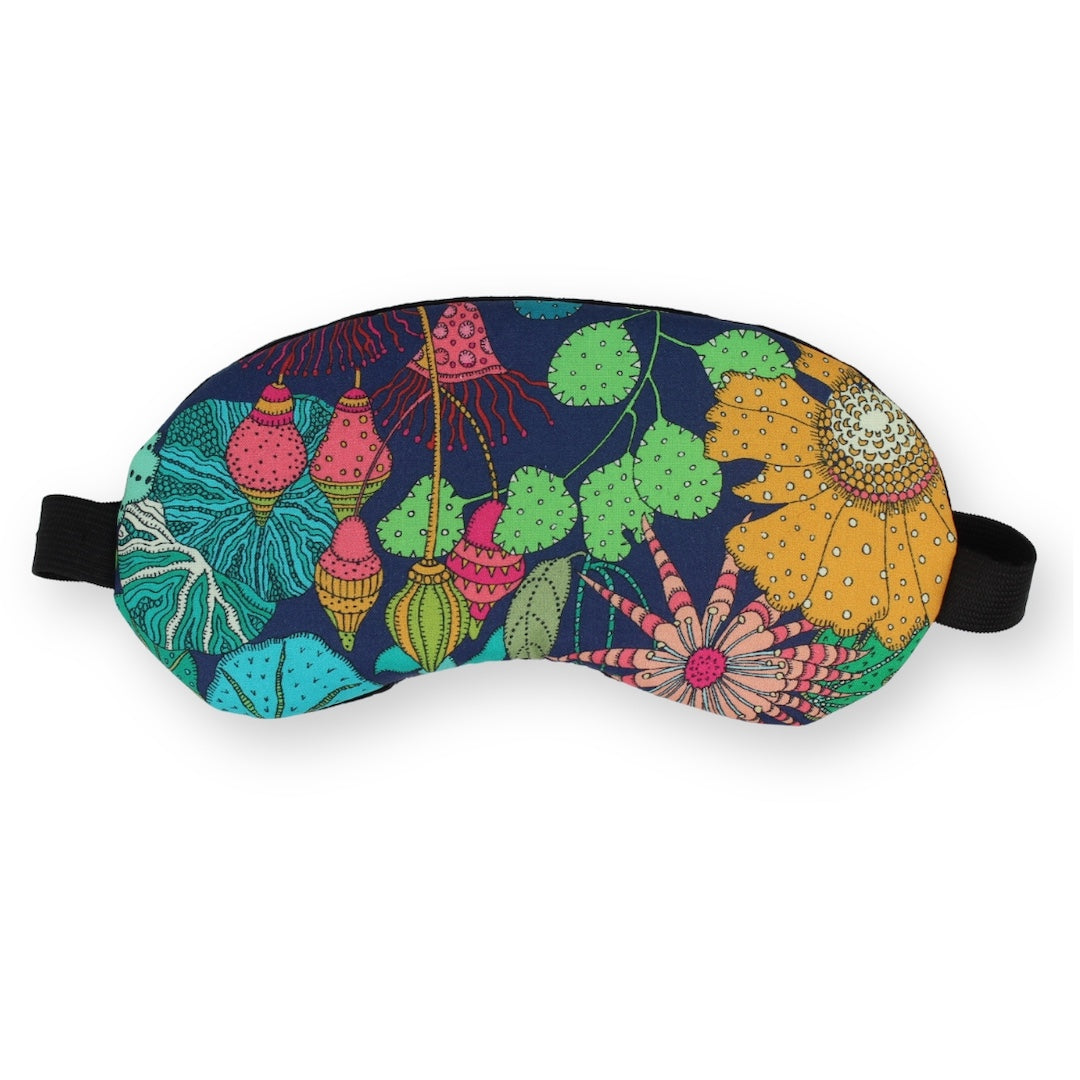 A sleep mask with a vibrant, multicolored botanical and floral pattern on a dark navy background, featuring black adjustable straps, shown against a plain white background.