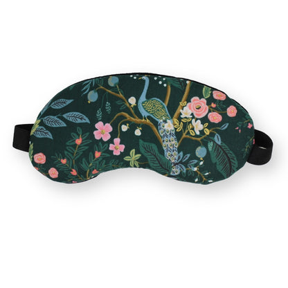 A dark green sleep mask with a detailed botanical and bird pattern featuring a peacock, pink flowers, and leaves, complete with an adjustable black strap, shown on a plain white background.