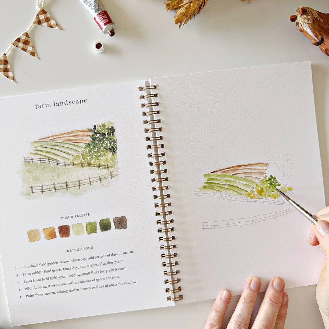 spiral bound workbook with a person painting a farm landscape with watercolors