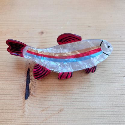 A fish shaped hair clip that has red, blue, and orange stripes down its center