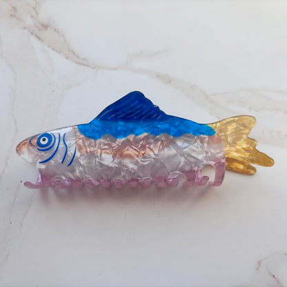 fish shaped hair clip with blue and gold colors on a white marble surface