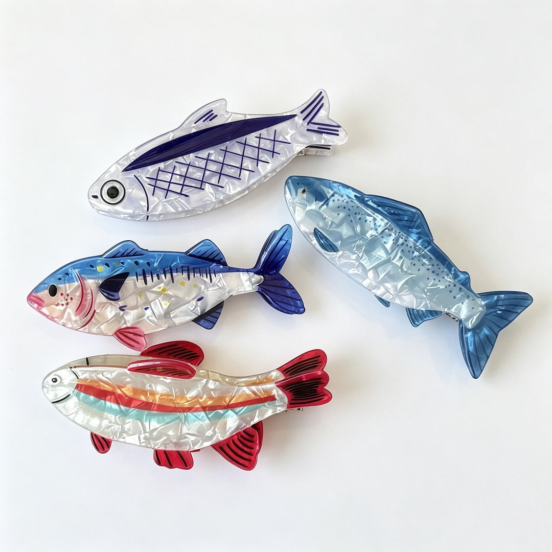 Four fish-shaped hair clips arranged on a plain white background, each with different color patterns including blue, red, orange, and white.