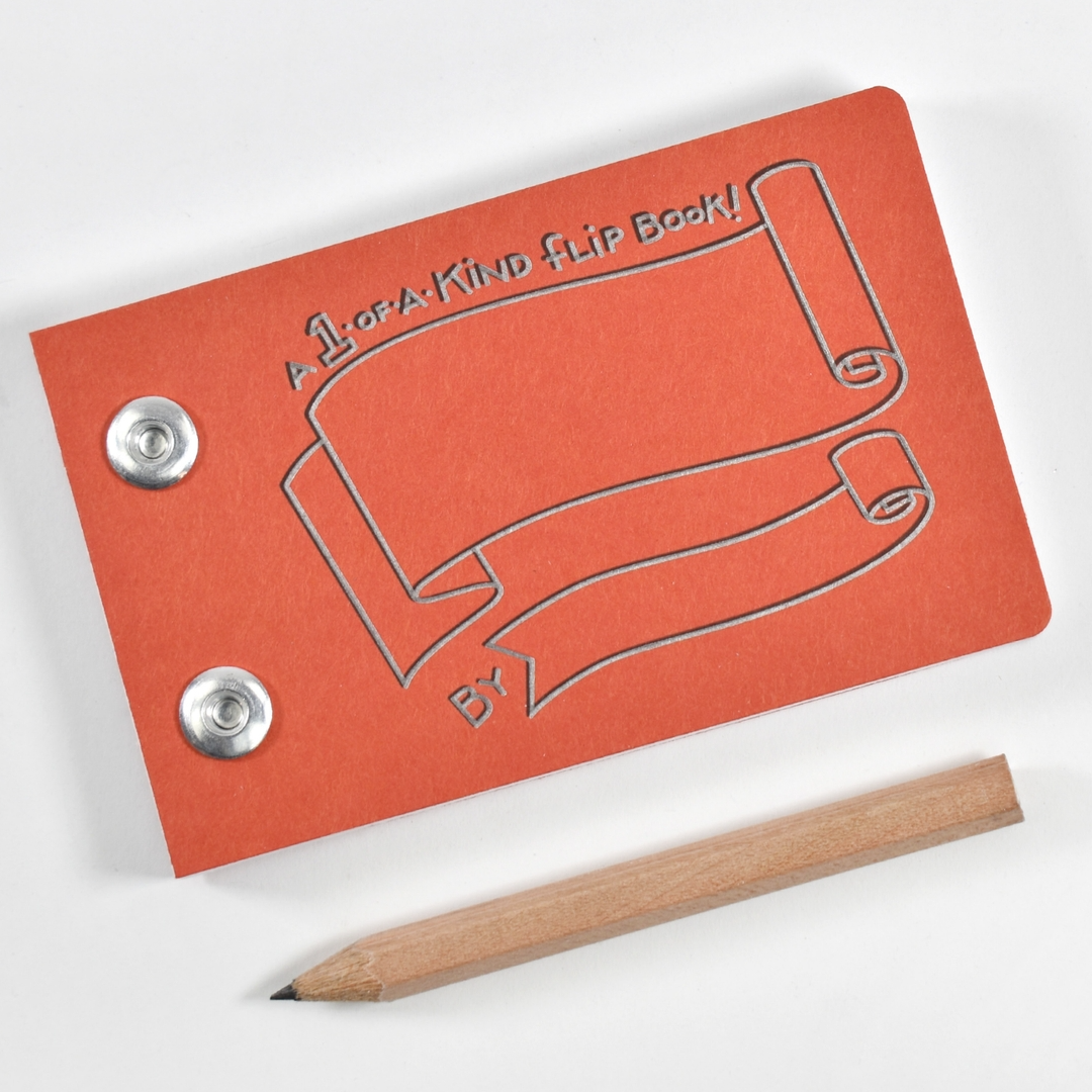 An orange-red flip book with embossed scroll artwork and two metal snap buttons, shown on a white background with a wooden pencil beside it.