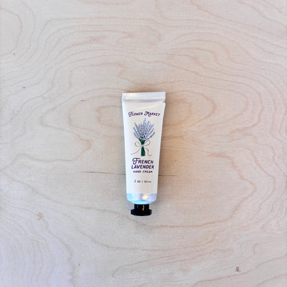 A squeeze tube of Flower Market French Lavender Hand Cream placed on a light wood grain surface.