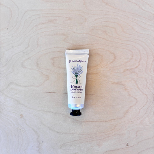 A squeeze tube of Flower Market French Lavender Hand Cream placed on a light wood grain surface.