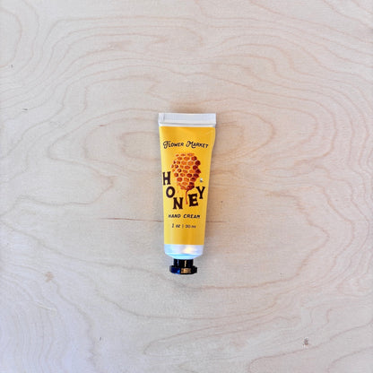 A squeeze tube of Flower Money Honey Hand Cream placed on a light wood grain surface.