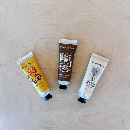 Three hand cream tubes from Flower Market are arranged on a light wood grain background. 