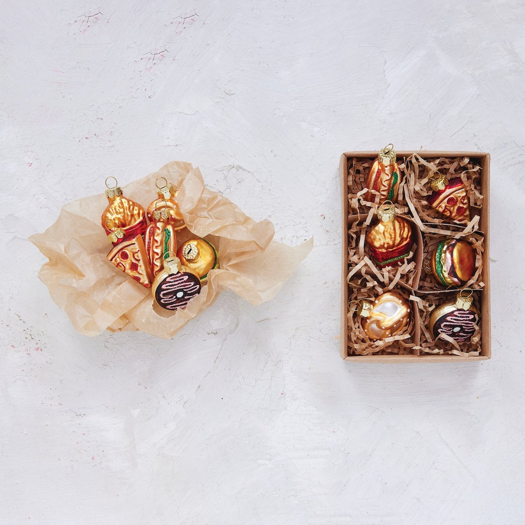  food themed Christmas ornaments in a box on a textured white surface