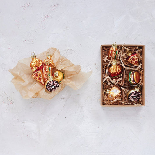  food themed Christmas ornaments in a box on a textured white surface