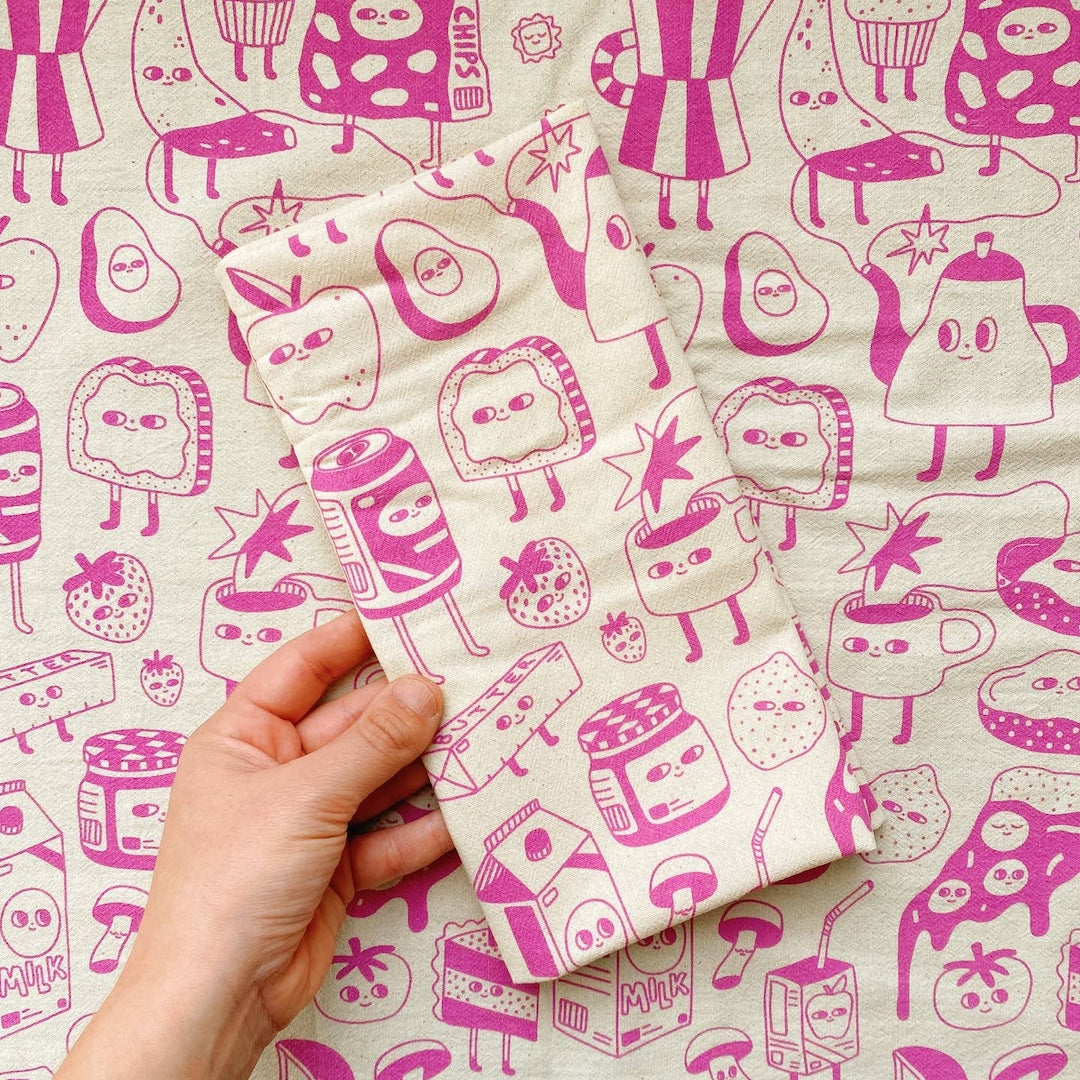 Hand holding a folded piece of dish towel with pink cartoon-style food illustrations on a matching background.