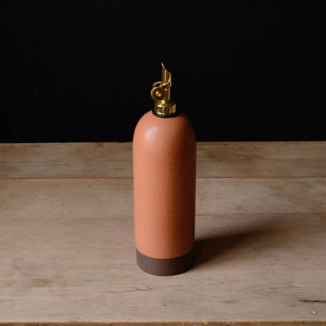 Pink ceramic oil cruet with gold cap on a wooden surface