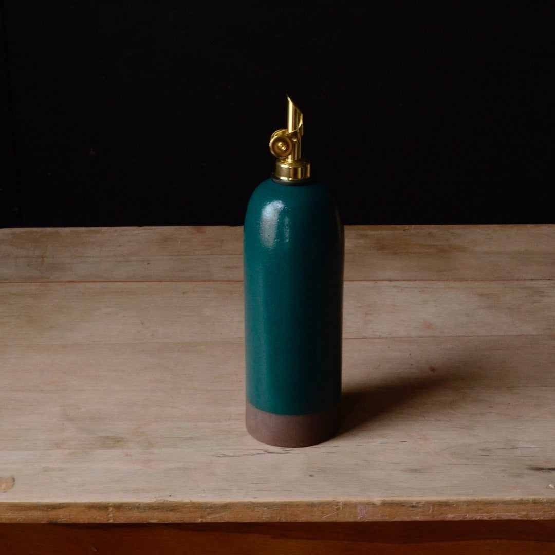 Teal oil cruet with a gold nozzle on a wooden surface