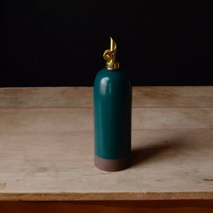 Teal oil cruet with a gold nozzle on a wooden surface
