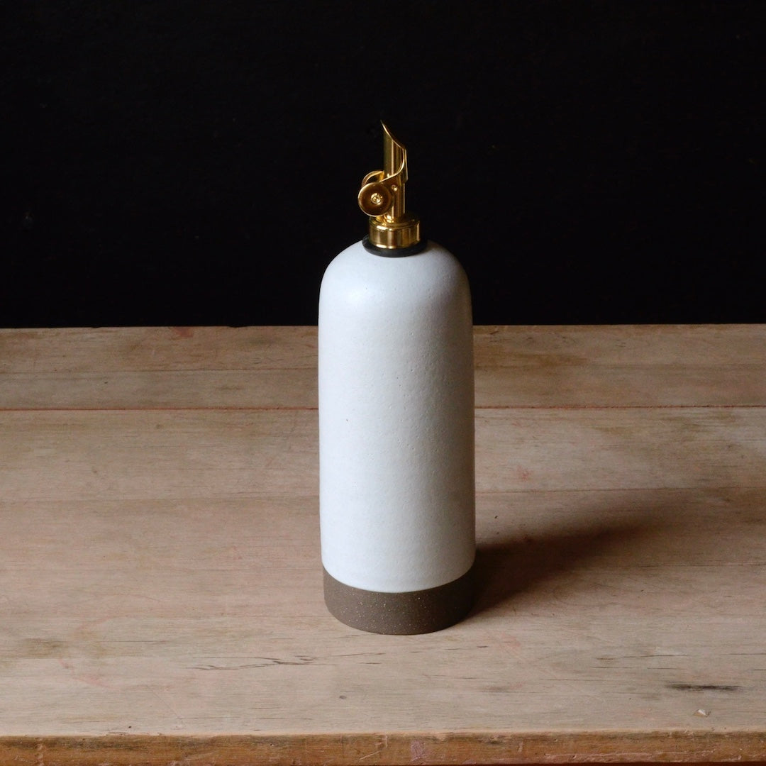 White ceramic oil cruet with gold nozzle on a wooden surface
