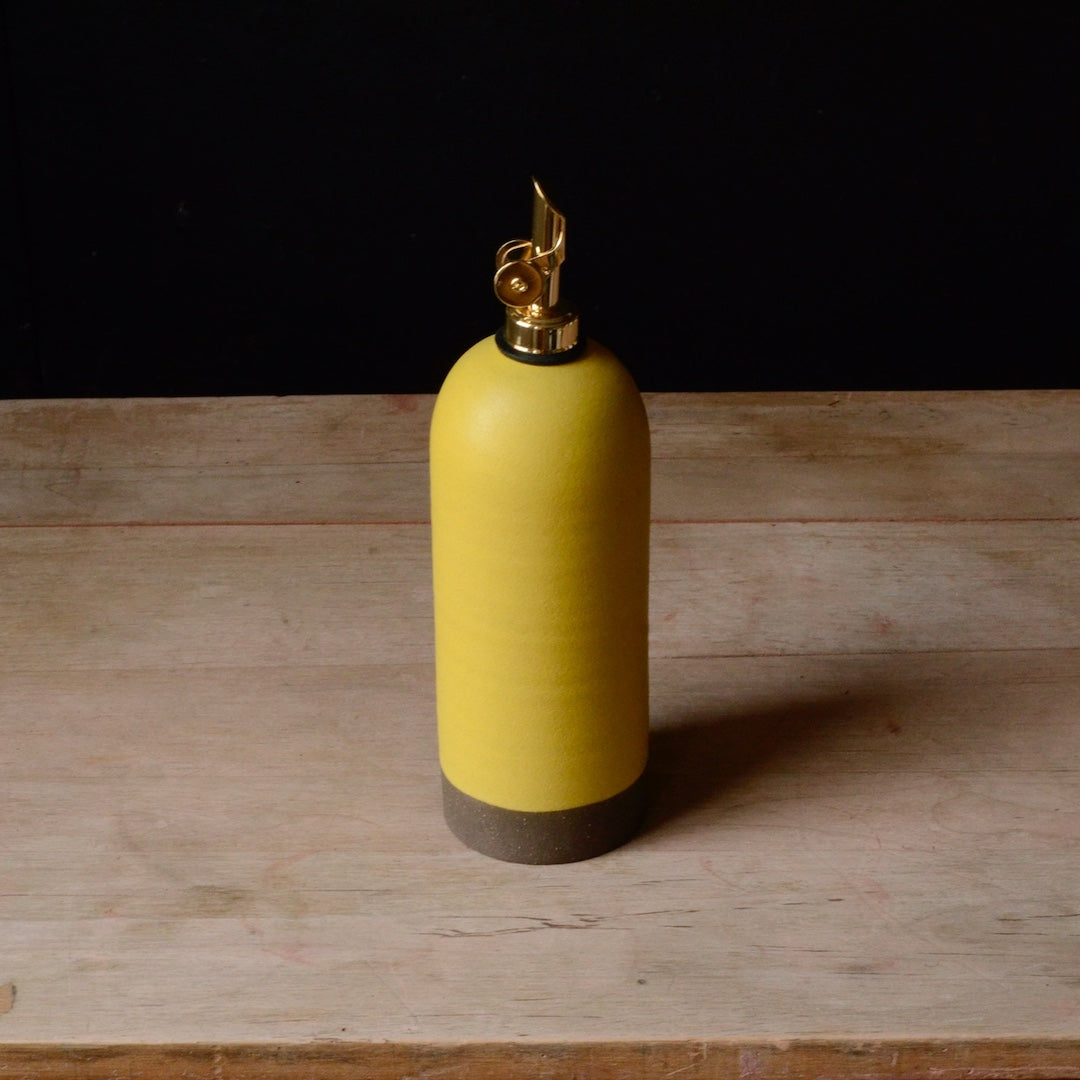 Yellow ceramic oil cruet with a gold nozzle on a wooden surface