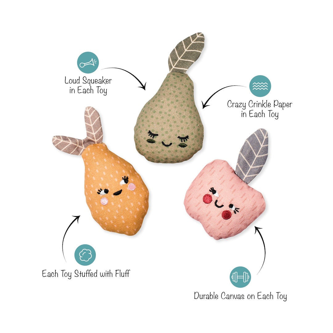Three plush puffer toys shaped like fruit, shown on a white background with callout arrows and text describing features: one pear in beige with green spots, one orange pear with pink cheeks, and one pink apple with red cheeks. Teal icons and labels mention loud squeaker, crazy crinkle paper, stuffed with fluff, and durable canvas.