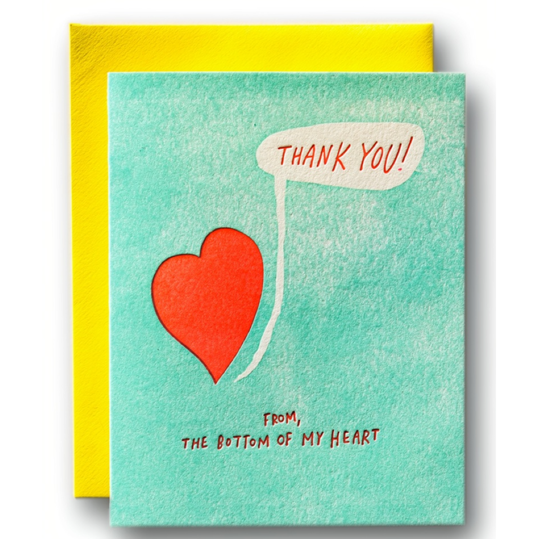 A square thank-you card with a textured mint green front and a bright yellow envelope behind it. The card features a red heart illustration, a white speech bubble reading 'THANK YOU!', and the phrase 'FROM, THE BOTTOM OF MY HEART' in red text.