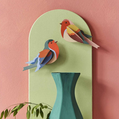 Decorative wall art with two colorful robins birds on a green board against a pink background