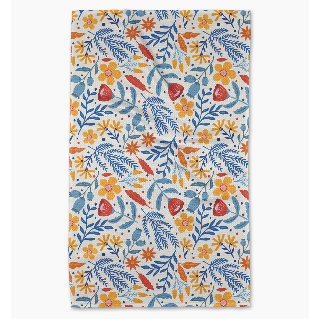 A rectangular kitchen towel with a dense botanical pattern featuring blue, orange, and red flowers and leaves on a cream background, shown flat against a light gray backdrop.
