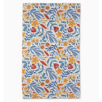 A rectangular kitchen towel with a dense botanical pattern featuring blue, orange, and red flowers and leaves on a cream background, shown flat against a light gray backdrop.