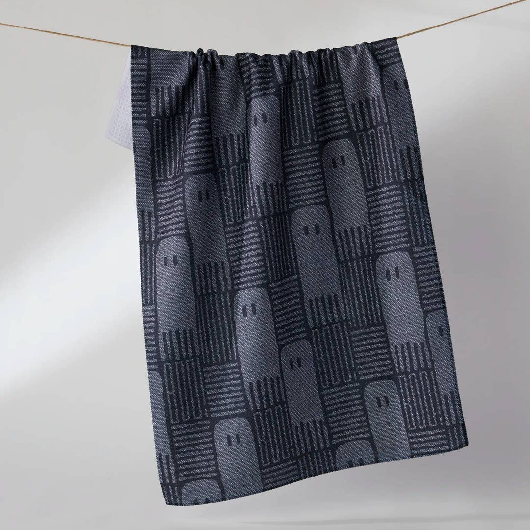 A dark gray kitchen towel with a repeating ghost pattern, hanging from a thin rope against a light gray background.