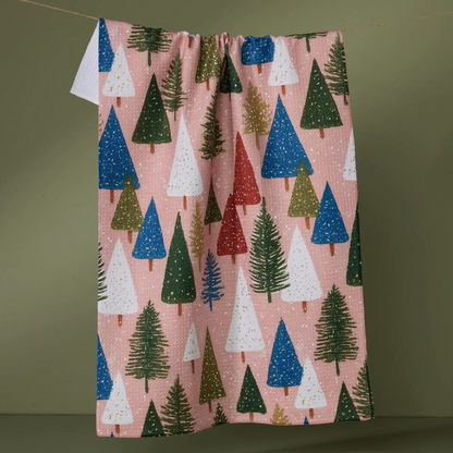 A pink kitchen towel with a repeating Christmas tree pattern in green, blue, white, and red, suspended against a plain olive-green background.