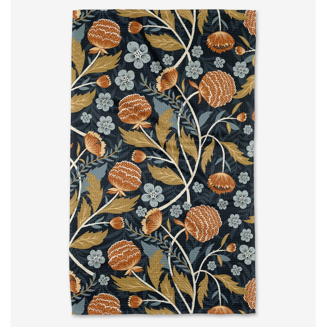 A tea towel with a dense botanical pattern, featuring orange-brown thistle-like flowers, muted gold leaves, and small pale blue blossoms on a dark navy background, shown flat against a light gray backdrop.