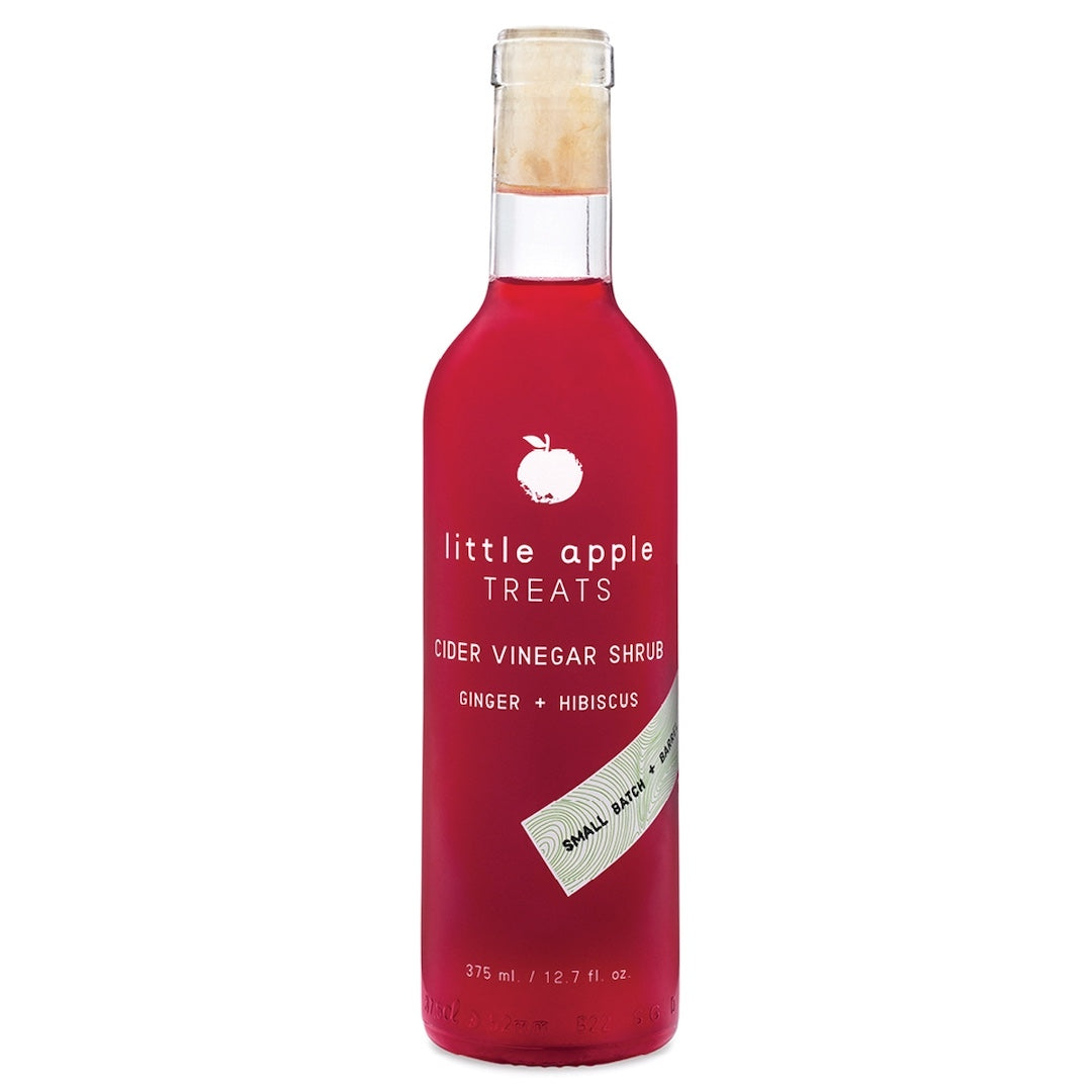 Red bottle of 'little apple treats' hibiscus ginger cider vinegar shrub with a white label on a white background