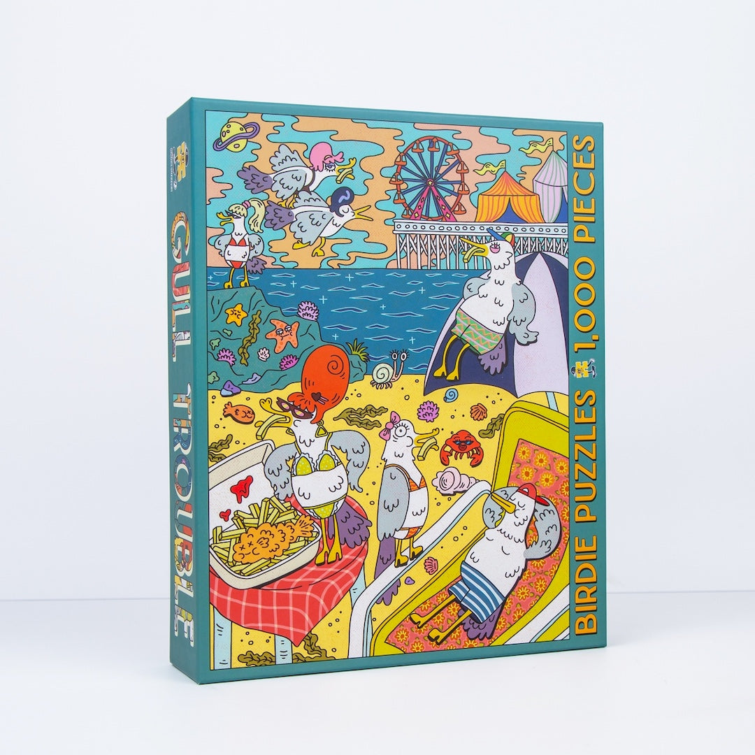 A boxed jigsaw puzzle titled 'Gull Treasure' with 1000 pieces, standing upright on a clean white background. The front and spine show a colorful cartoon illustration of gulls at a beach with a Ferris wheel, food, and playful seaside scenes.