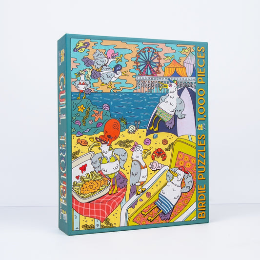 A boxed jigsaw puzzle titled 'Gull Treasure' with 1000 pieces, standing upright on a clean white background. The front and spine show a colorful cartoon illustration of gulls at a beach with a Ferris wheel, food, and playful seaside scenes.