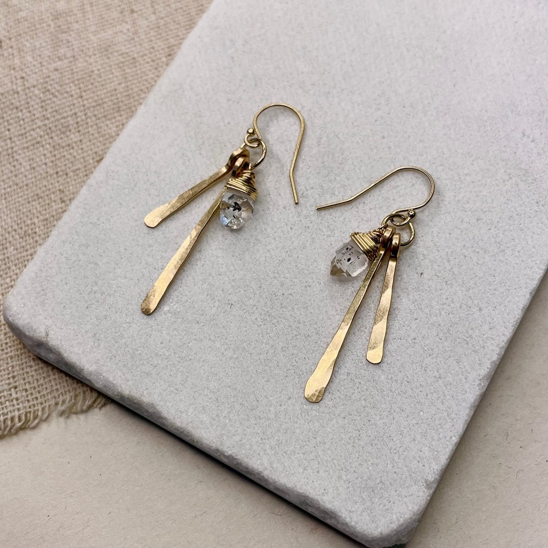 Gold earrings with herkimer diamond dangles on a textured stone surface
