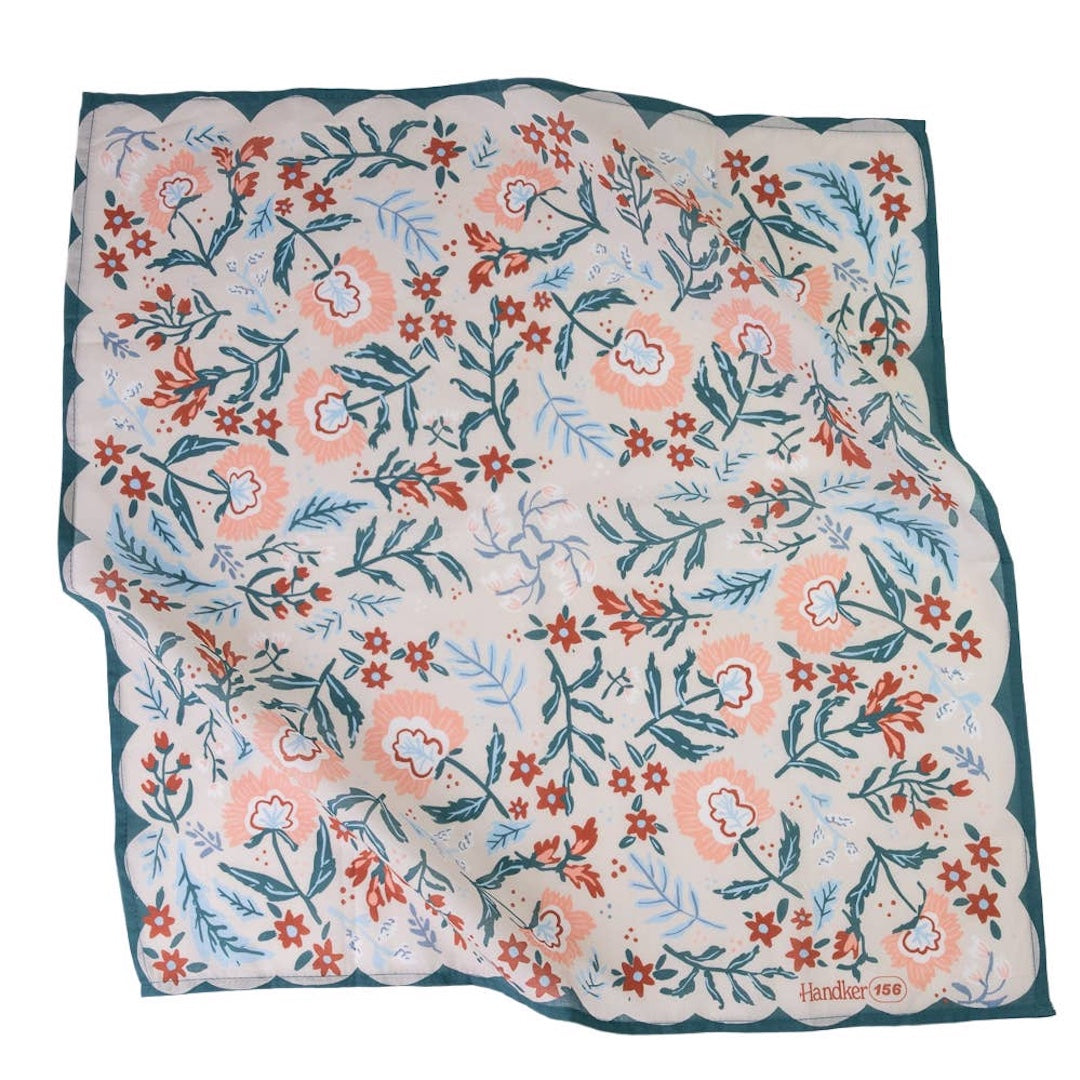 A bandana featuring a hand-drawn style floral pattern in coral pink, rust red, and light blue on a cream background, finished with a dark teal border.